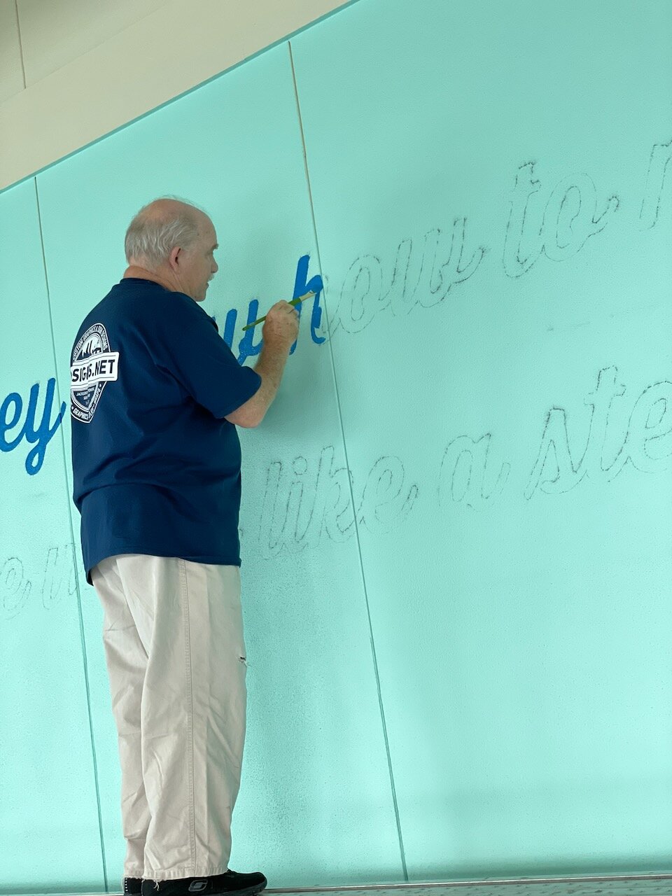 CG Signs designer hand-sketching script lettering on a glass interior wall